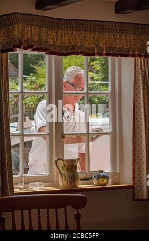 Hampshire, Angleterre, Royaume-Uni. 2020. Peintre décorateur peinture de petites fenêtres sur une maison rurale vue de l'intérieur de la maison. Banque D'Images