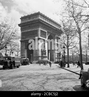 Années 1950, historique, activité à l'Arc de Triomphe de l'Etoile, montrant la circulation et les bus en attente sur la rue pavée menant à l'arche géante. L'un des monuments de la ville, commandé par Napoléon Ier, est situé au centre de la place Charles de Gaulle, à l'extrémité ouest des célèbres champs-Elysées, Paris, France. Banque D'Images