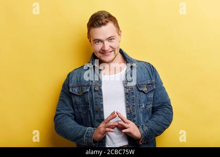 beau homme tenant le doigt au doigt avec une expression sérieuse regardant l'appareil photo debout sur fond jaune, plan, idée. portrait gros plan Banque D'Images
