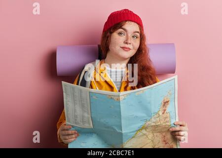 sourire positif gingembre touriste tenant une carte, prenant la décision où voyager, photo de gros plan. isolé fond rose, studio tourné. personnes, passe-temps, Banque D'Images