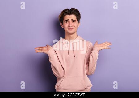 Portrait en gros plan d'un jeune homme sans indice et perplexe portant un sweat-shirt rose, bras dehors se demandant pourquoi quel est le problème qui se soucie si, Je ne sais pas. Isola Banque D'Images