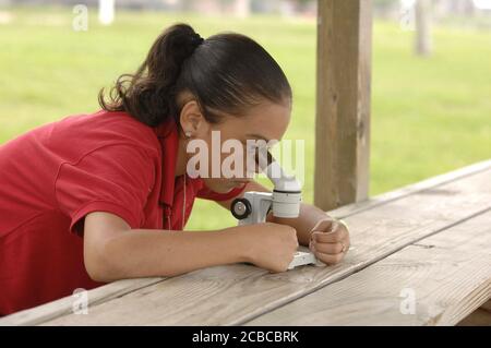 Granite Shoals, Texas, États-Unis, 1 mai 2007 : les étudiants de l'IDEA Academy, une école secondaire publique de Brownsville, vivent un camp d'éducation en plein air de trois jours pour favoriser le leadership et la croissance personnelle. Une fille hispanique regarde à travers un microscope pour les micro-organismes dans un échantillon d'eau du lac voisin. ©Bob Daemmrich Banque D'Images