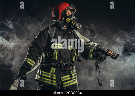 brave pompier éteindre le feu dans la fumée, en utilisant l'équipement spécial et en portant l'uniforme et le casque Banque D'Images