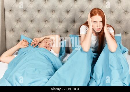 Agacé femme malheureuse bloquant ses oreilles du bruit de son mari ronflant dans la chambre à la maison. Gros plan photo. Concept de frustration Banque D'Images