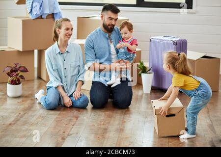 La famille de quatre hommes s'assoit à l'étage dans la chambre d'hôtes de la maison de vente. La fille aînée porte un t-shirt jaune pousse boîte. Maman sourire. Papa garde la fille la plus jeune Banque D'Images