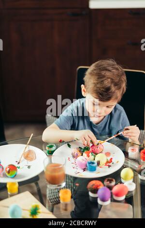 Mignon petit mâle peinture pour enfants des oeufs de Pâques dans des couleurs différentes, cette activité lui permet de tomber dans l'atmosphère de fête de Pâques Banque D'Images