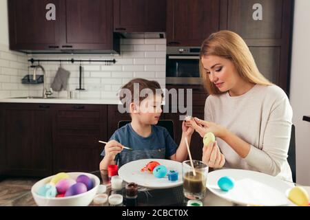 Happy blonde mère et son fils de quatre ans faire des oeufs de Pâques, bénéficiant de temps libre passé ensemble à la maison. Célébrer Pâques en famille. Parent Banque D'Images