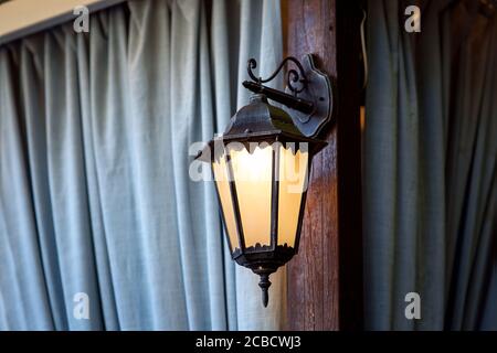 Lanterne de rue forgée en métal noir montée sur un arbre en bois sur le fond de rideaux de tissu bleu, gros plan. Banque D'Images