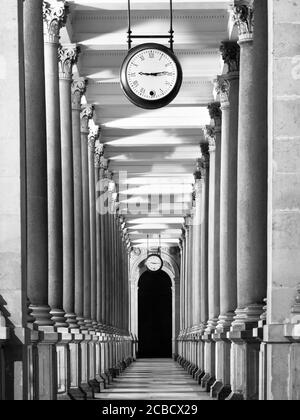 Long couloir de colonnafe avec colonnes et horloge accrochées au plafond. Perspective du cloître. . Image en noir et blanc. Banque D'Images