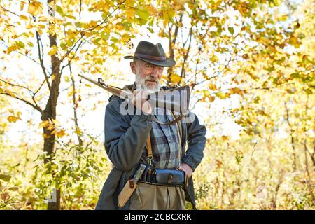 Un chasseur satisfait porte un fusil à l'épaule, regardant caméra.automne nature arrière-plan. Concept de chasse masculin, de loisir et de loisir Banque D'Images