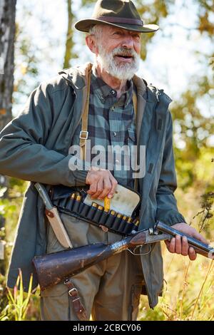 Senior fowler tenant le fusil de chasse, les cartouches sur le bas du dos, prêt à tirer sur les oiseaux. Arrière-plan de la forêt Banque D'Images