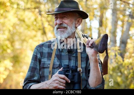 Rire, sourire chasseur senior avec fusil de chasse sur l'épaule et jumelles dans les mains Banque D'Images