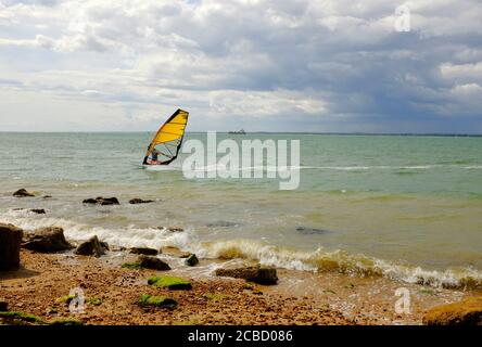 Planche à voile avec voiles colorées naviguant sur le Solent au large de Gurnard front de mer de l'île de Wight dans une brise raide sous un ciel atmosphérique Banque D'Images