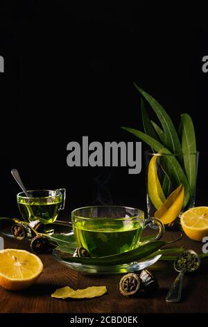 Verre de thé vert chaud sur une table en bois avec des feuilles d'eucalyptus, des feuilles de Laurier, des épices telles que l'origan et les citrons. Ingrédients et produits naturels. Banque D'Images