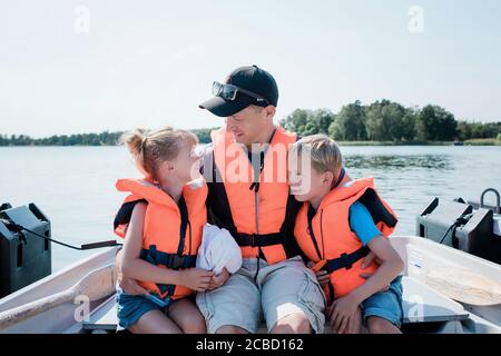 le père s'est assis en train d'embrasser ses enfants sur un bateau à rames Été en Suède Banque D'Images