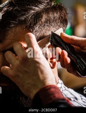 Concept de coupe de cheveux. Homme en visite chez le coiffeur dans le salon de coiffure. Mains du coiffeur avec tondeuse cheveux, gros plan. Homme barbu dans un salon de coiffure Banque D'Images