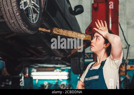 Égalité des sexes. Une jeune femme brune en uniforme se tient près de l'ascenseur avec la voiture, et regarde la roue, essuyant la sueur de son front. En t Banque D'Images