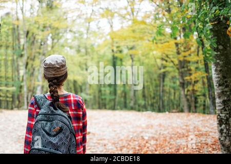 Une jeune femme caucasienne pose avec un sac à dos sur son dos. La vue de l'arrière. En arrière-plan, arbres et forêt. Concept de voyage et de tourisme. Banque D'Images