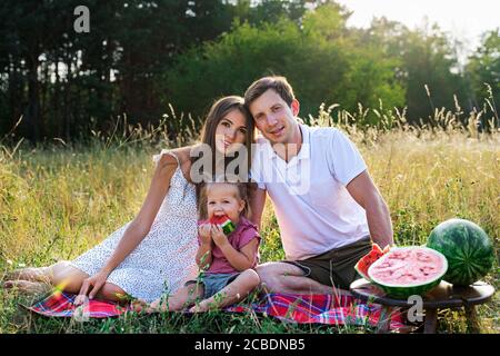 belle famille, maman, papa et fille assis sur un pique-nique avec la pastèque. Banque D'Images