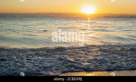 Le soleil raye à travers les nuages au lever du soleil avec des vagues dorées sur la plage. Illustration de l'idée que l'espoir est à l'horizon. Banque D'Images