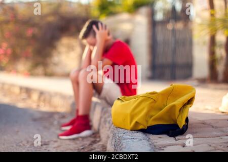 Élève malheureux avec sac à dos assis à l'extérieur. Le garçon ressent du stress. Enfants et émotions concept Banque D'Images