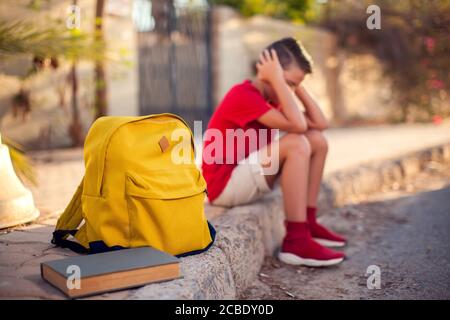 Élève malheureux avec sac à dos assis à l'extérieur. Le garçon ressent du stress. Enfants et émotions concept Banque D'Images