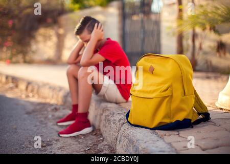 Élève malheureux avec sac à dos assis à l'extérieur. Le garçon ressent du stress. Enfants et émotions concept Banque D'Images