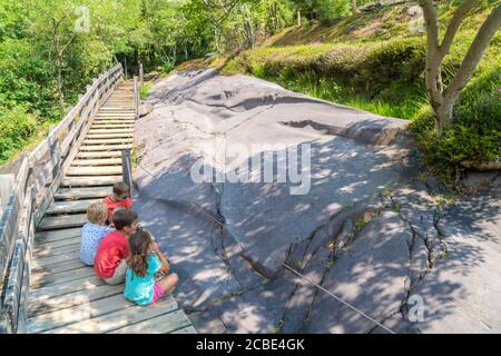 Enfants regardant des dessins rupestriens sculptés sur des rochers, Parc Naquane, Capo di Ponte, Valcamonica, Lombardie, Italie Banque D'Images