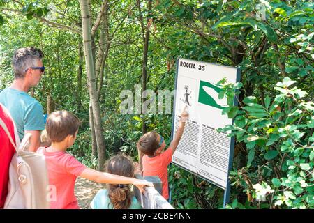 Père avec enfants regarde le panneau d'information au Parc National de Naquane de Rupestrian gravures, Valcamonica, Lombardie, Italie Banque D'Images