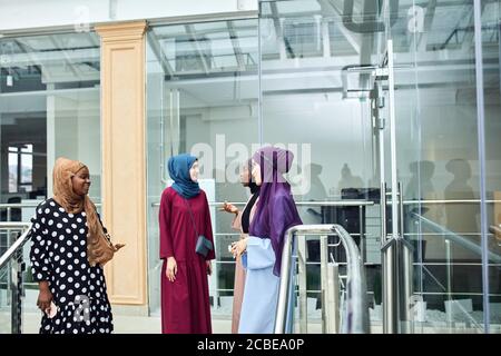Groupe de femmes musulmanes souriantes dans le hijab marchant dans les escaliers du centre d'affaires. Les femmes arabes et africaines vêtues de robes longues et élégantes et de foulards Banque D'Images