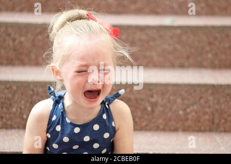 petite fille dans une robe bleue est assis sur les marches et pleure Banque D'Images