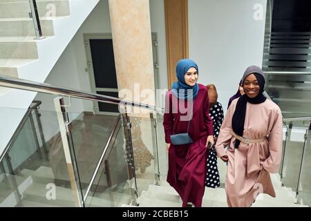 Groupe multiracial de femmes d'affaires musulmanes visitant la conférence internationale au centre d'affaires, marchant dans l'escalier partageant des impressions et des idées Banque D'Images