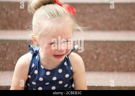 petite fille dans une robe bleue est assis sur les marches et pleure Banque D'Images