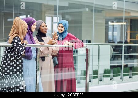 Groupe de femmes d'affaires musulmanes multiraciales qui discutent, qui vérifient les actualités sur leur smartphone tout en faisant une pause, se tenant au centre d'affaires Banque D'Images