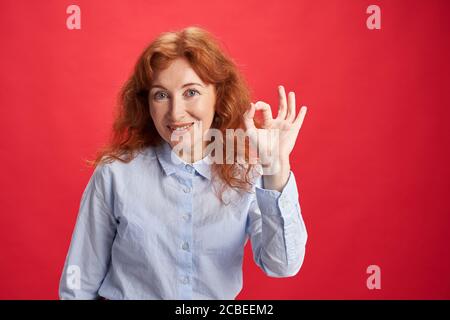 Femme souriante et rouge, montrant le signe OK avec sa gauche main sur l'arrière-plan rouge Banque D'Images