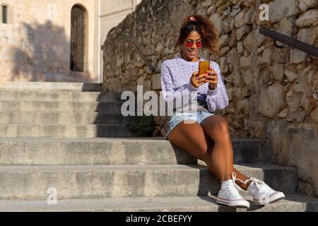 Portrait d'une jeune femme noire attrayante prenant un selfie avec son mobile. Parler au téléphone, assis dans les escaliers Banque D'Images