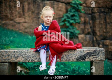 une jeune fille sur un banc est enveloppée dans une couverture en laine. Banque D'Images