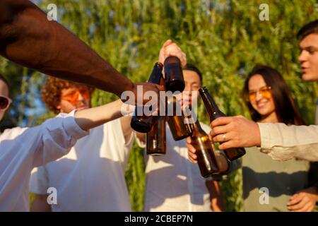 Santé. Groupe d'amis qui se trinquent des verres de bière pendant le pique-nique à la plage au soleil. Style de vie, amitié, s'amuser, week-end et concept de repos. Elle est gaie, heureuse, festive, festive. Banque D'Images