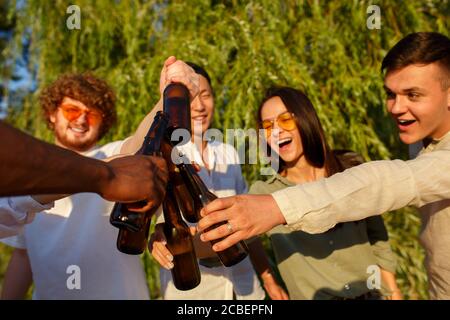 Santé. Groupe d'amis qui se trinquent des verres de bière pendant le pique-nique à la plage au soleil. Style de vie, amitié, s'amuser, week-end et concept de repos. Elle est gaie, heureuse, festive, festive. Banque D'Images