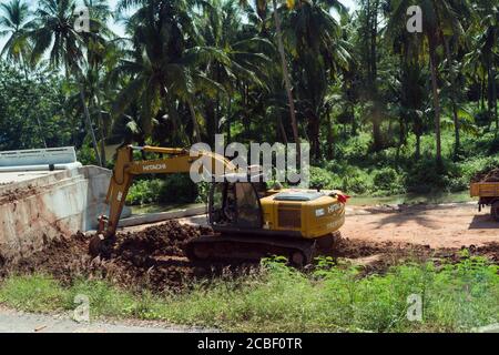 THAÏLANDE, PHUKET - 15 décembre 2019 : une pelle hydraulique est debout dans la boue. Pelle hydraulique sur un chantier de construction de routes avec des palmiers en arrière-plan. Banque D'Images