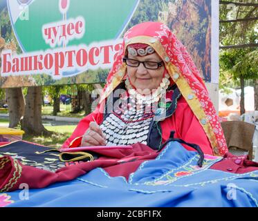 Ekaterinbourg, Russie, 15 juin 2019. Une femme âgée vêtue de Bashkir brode un motif en crochet. Fête nationale traditionnelle Sabantuy dans le c Banque D'Images