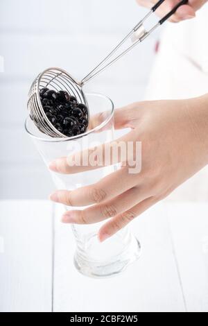 Faire du thé moussant, verser et verser des boules de tapioca de sucre brun cuites dans une tasse sur fond blanc de table en bois, gros plan, copier l'espace Banque D'Images