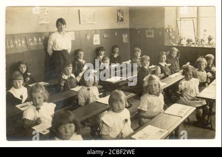 Carte postale de l'époque de la première Guerre mondiale des écoliers tenant des fleurs, en classe avec un enseignant, vers 1915, Royaume-Uni Banque D'Images