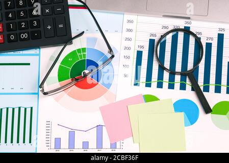 Loupe, lunettes, calculatrice et notes adhésives sur votre bureau. Graphiques statistiques avec des nombres. Documents financiers avec données commerciales Banque D'Images