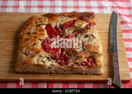 Un grand morceau de foccacia fraîchement cuit, recouvert de poivrons rouges, d'oignons, de graines de sésame et de romarin Banque D'Images