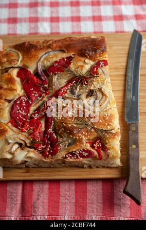 Un grand morceau de foccacia fraîchement cuit, recouvert de poivrons rouges, d'oignons, de graines de sésame et de romarin Banque D'Images