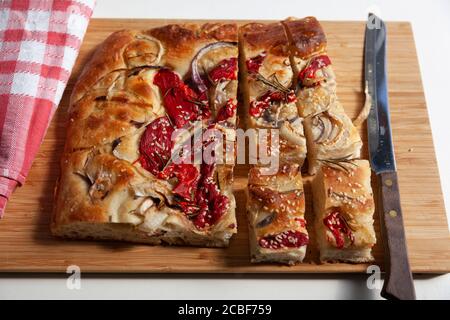 Un grand morceau de foccacia fraîchement cuit, recouvert de poivrons rouges, d'oignons, de graines de sésame et de romarin Banque D'Images