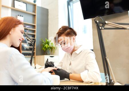 Une fille souriante positive en chemise est venue au salon pour faire de la manucure. Chemise blanche sur manucure Banque D'Images