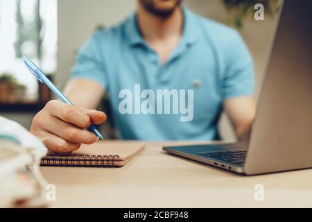 Des étudiants de sexe masculin font des études à domicile pendant la quarantaine. Gros plan d'une table avec un ordinateur portable, des carnets et un masque médical Banque D'Images
