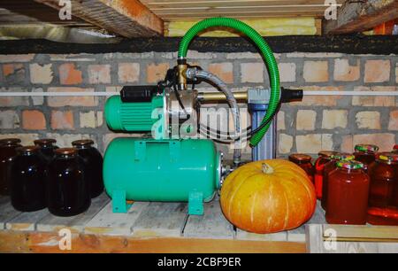 Compresseur électrique avec moteur sur une étagère dans le sous-sol de la maison, à côté de pots en verre pour stocker les jus de fruits et de baies en conserve. Banque D'Images